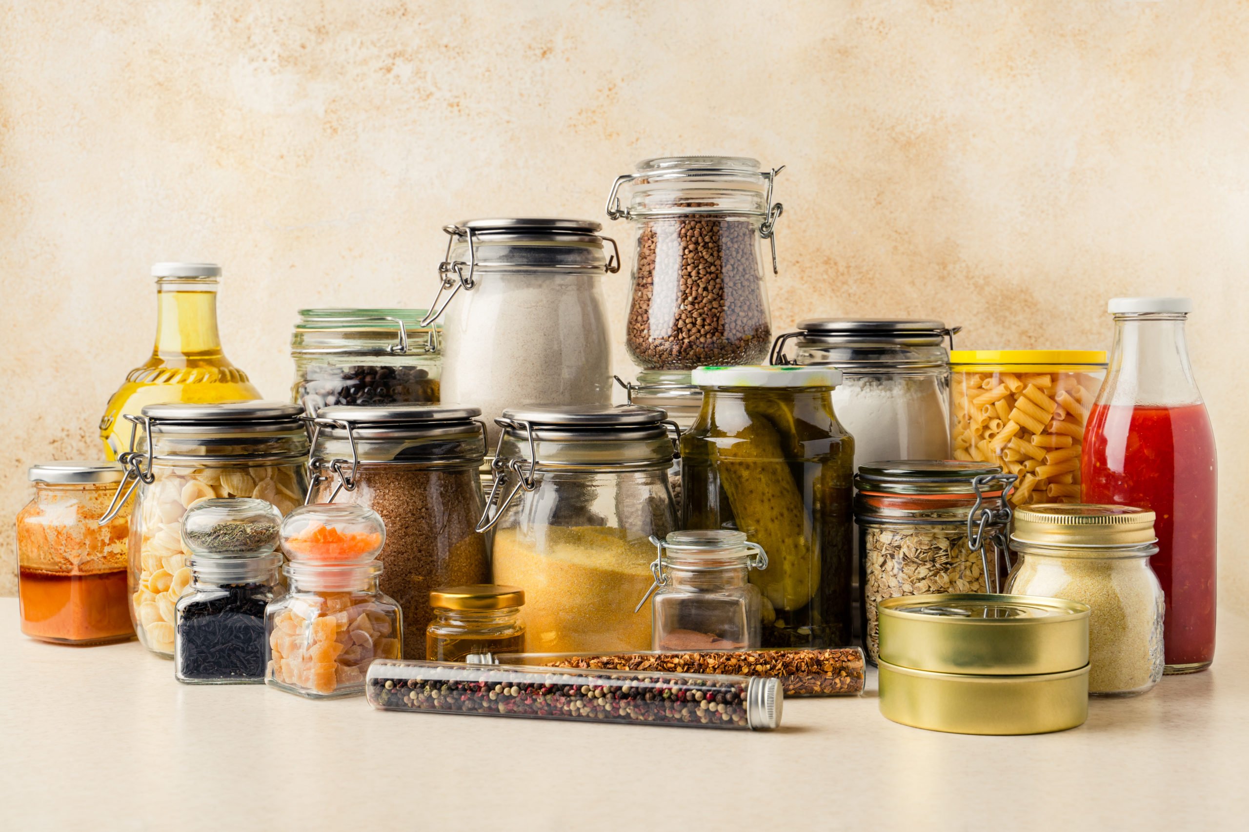 Various food supplies including grains, condiments, tomato sauce, oil in glass bottles and jars, dry pasta, canned produce on kitchen table. Sustainability concept. Horizontal orientation